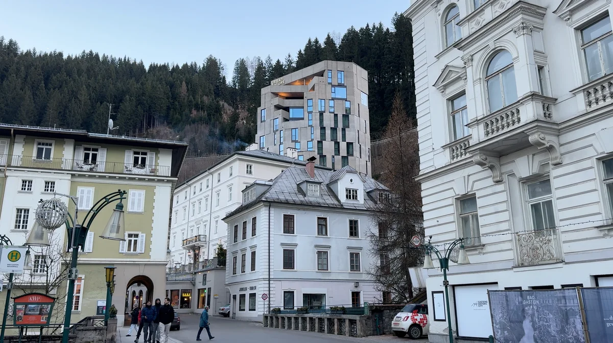 Historic facades and a modern building on the wooded slope above a square in Bad Gastein.