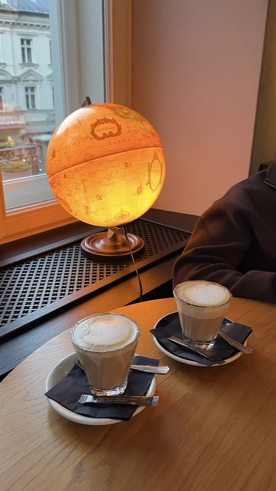 Two glasses of milky coffee on a wooden table beside an illuminated globe and a window.