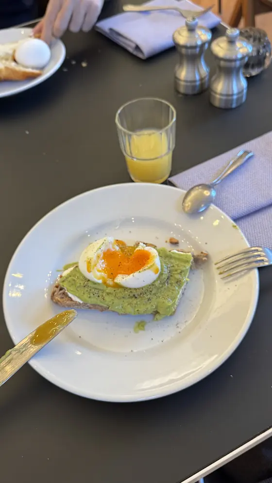 Toast with an avocado spread and a soft-boiled egg on a white plate beside a glass of juice.