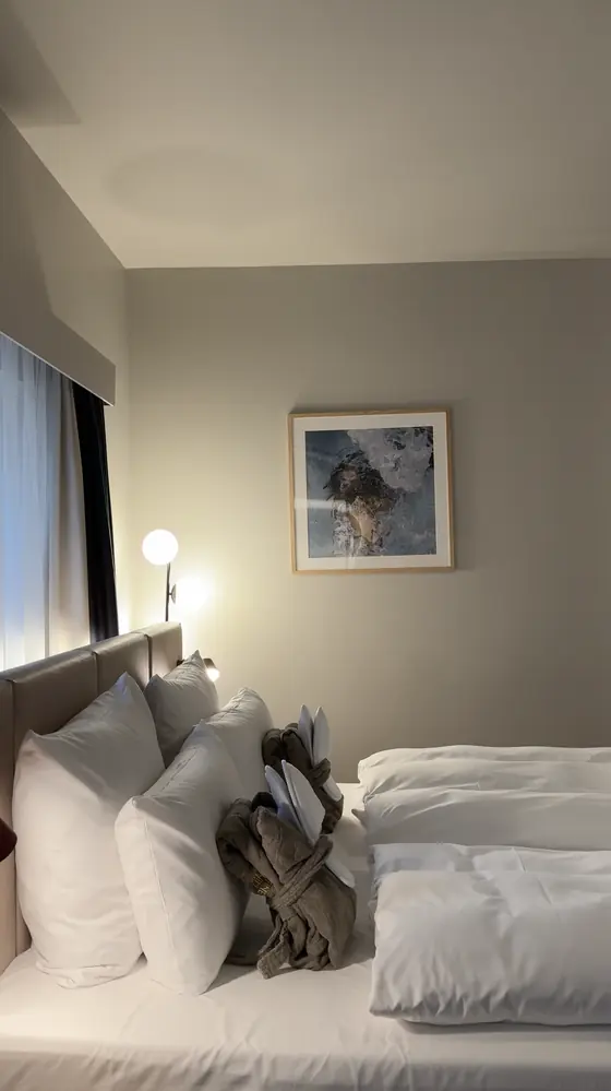 Side view of the bed, folded robes, a floor lamp and framed artwork in our junior suite.