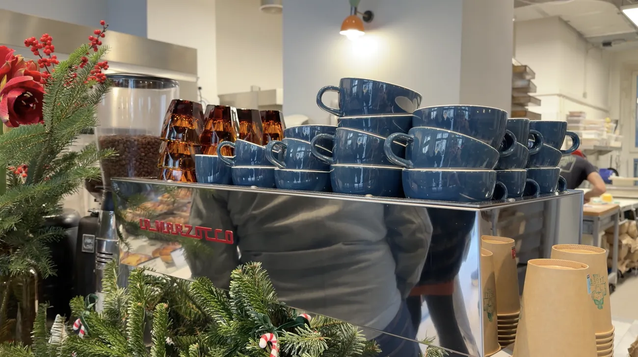 A coffee machine with stacks of blue cups, paper cups and Christmas greenery.
