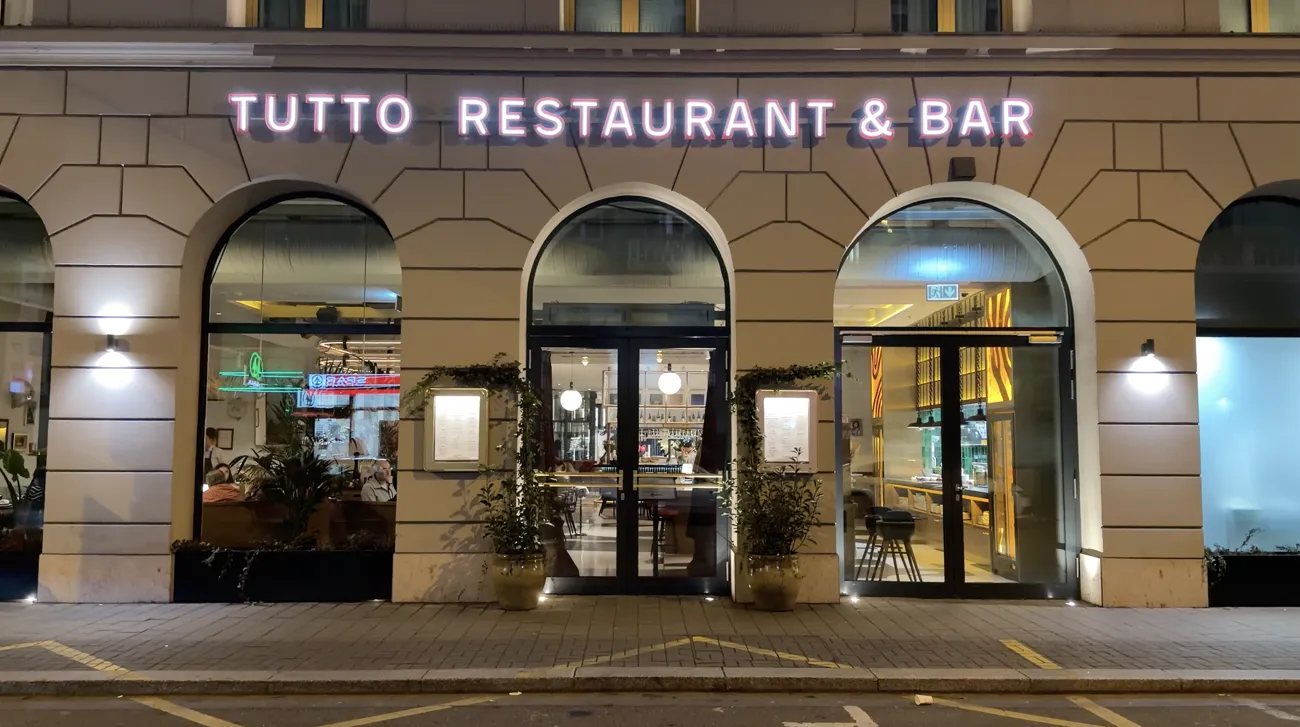 The illuminated Tutto Restaurant & Bar sign above arched windows at night.