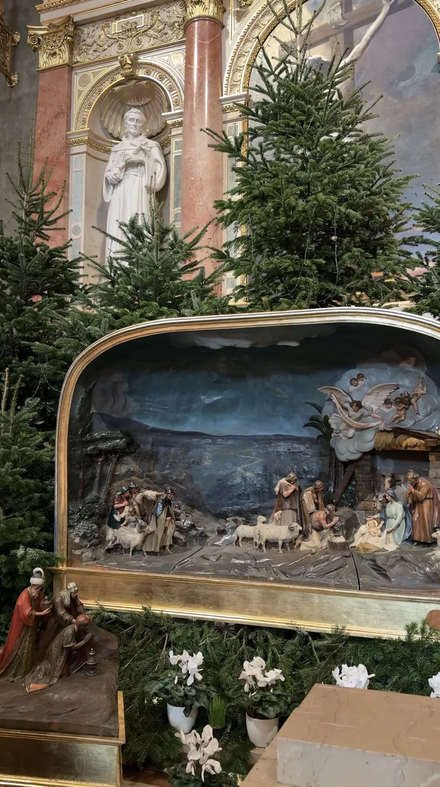 A nativity scene with small figures beside Christmas trees inside the basilica.