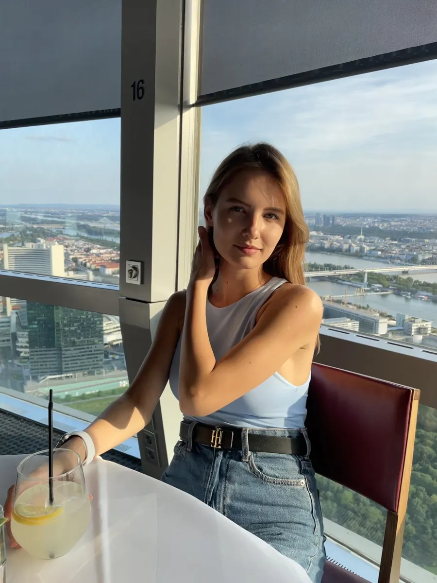 A woman at a window table with a lemon-garnished drink and Vienna in the background.