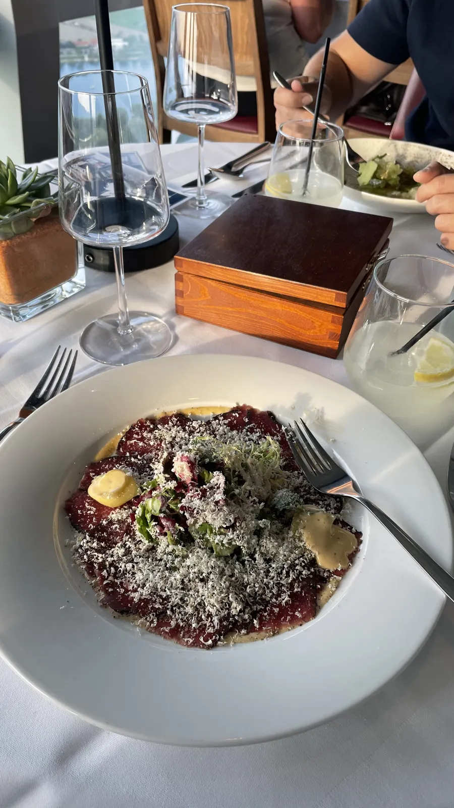 A plate with thin red slices, grated topping, greens and sauce at the restaurant table.