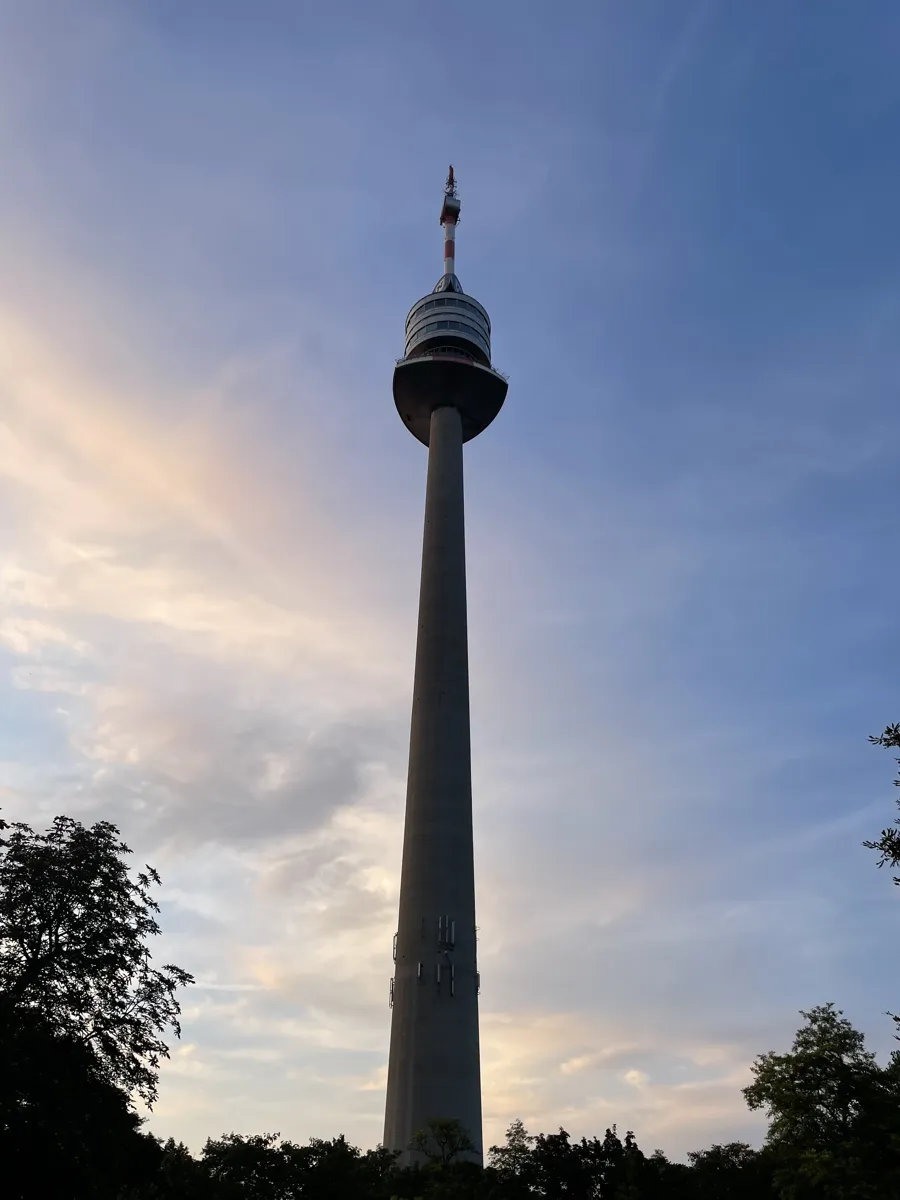 The Donauturm tower rising above trees against a pale blue and pink sky.