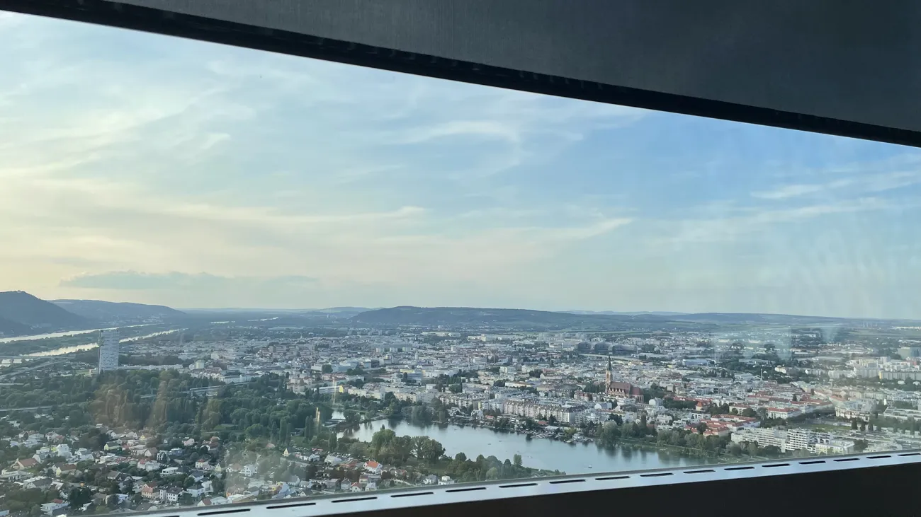 Wide panorama of Vienna, water, trees and distant hills through the restaurant window.