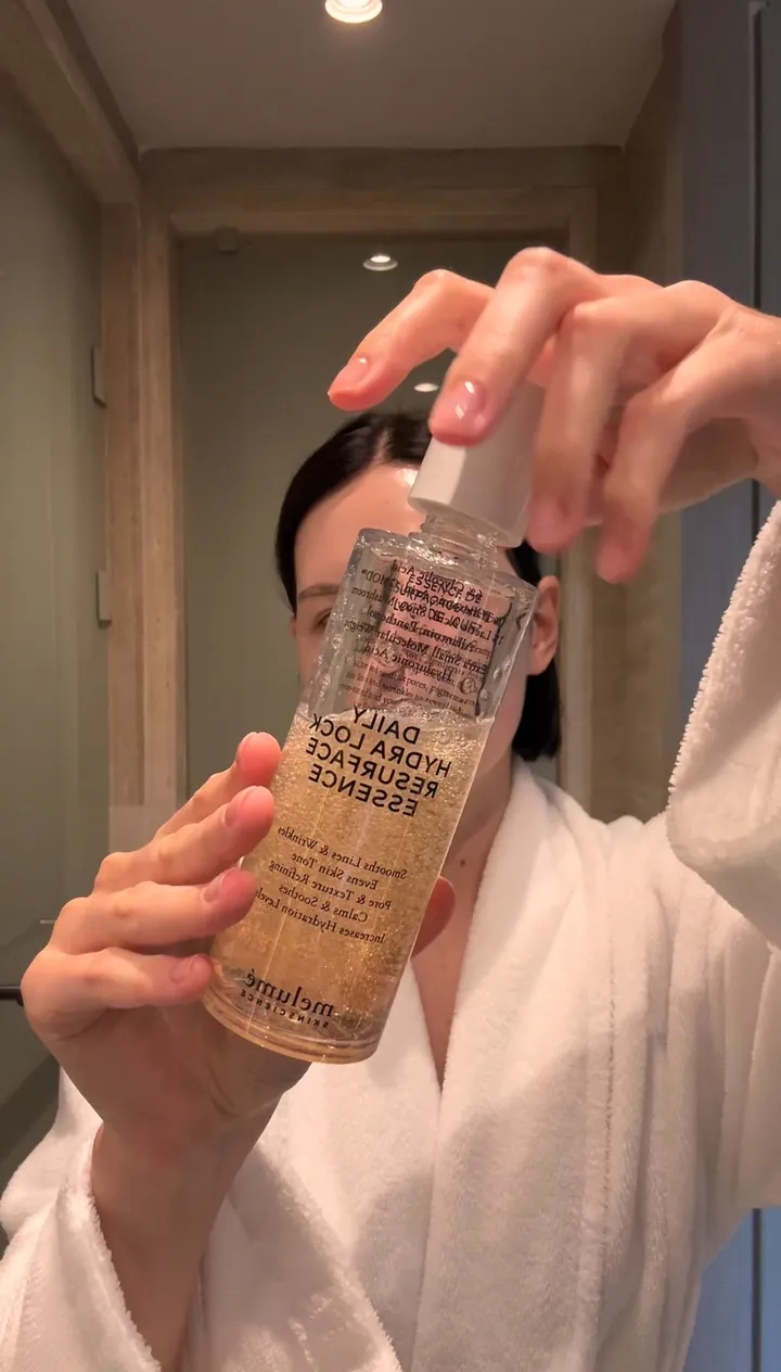 A hand holding a bottle of Melumé Daily Hydra Lock Resurface Essence.