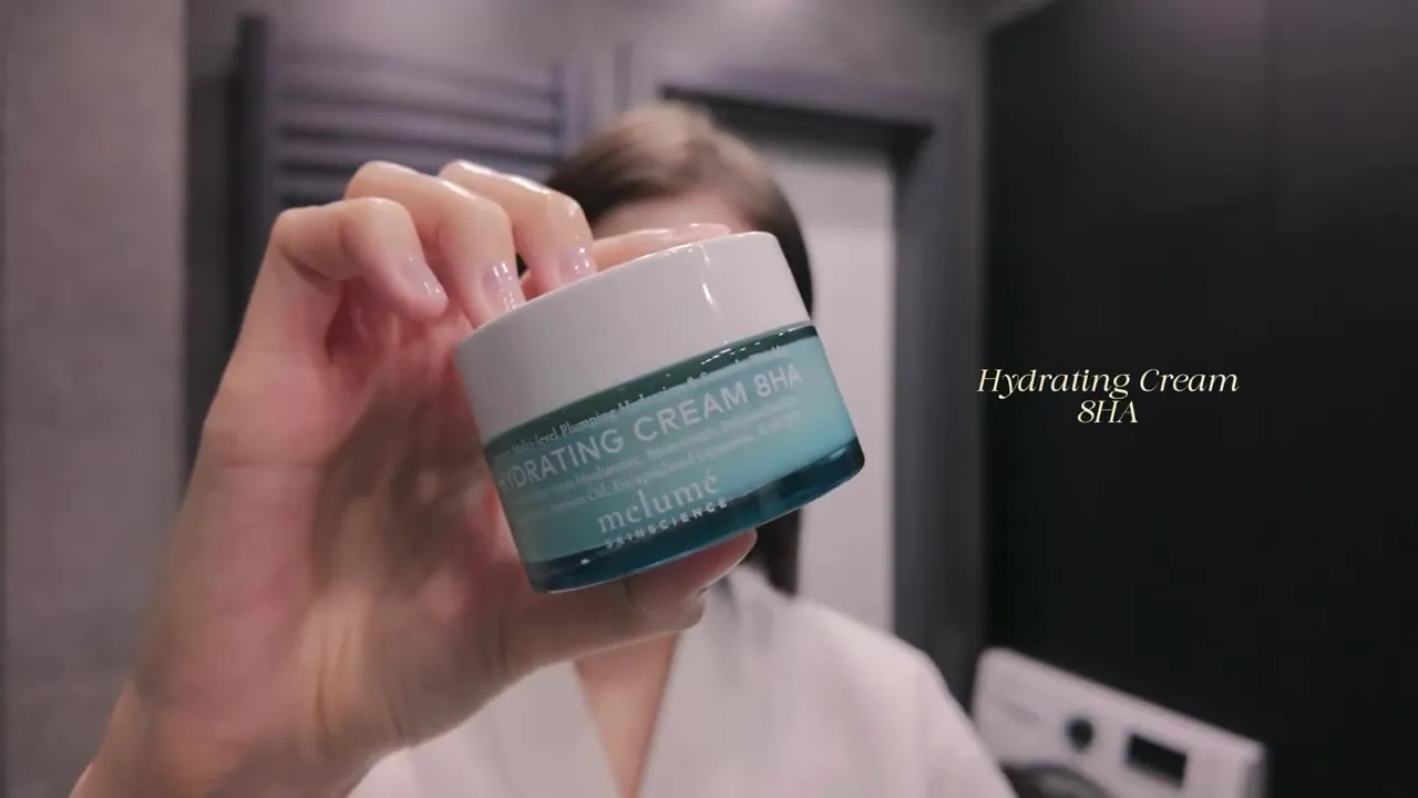 A hand holding a blue jar of Melumé Hydrating Cream 8HA with a white lid.
