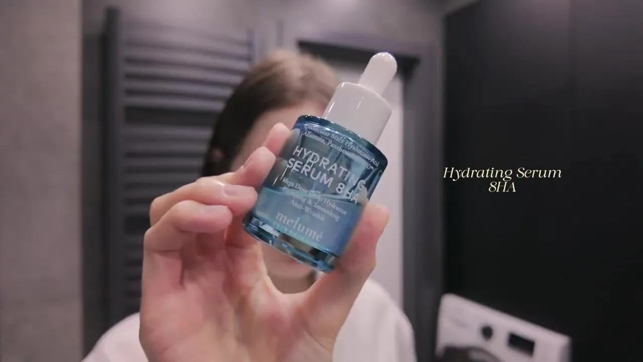 A hand holding a blue dropper bottle of Melumé Hydrating Serum 8HA.