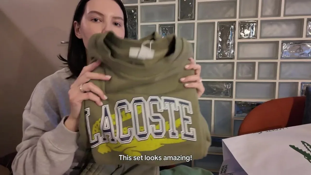 Me holding the olive top from the Lacoste set, with large lettering and a yellow crocodile.
