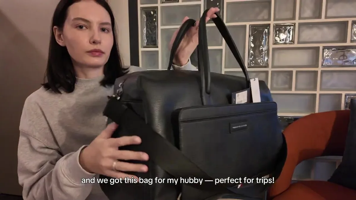 Me holding a large black Tommy Hilfiger travel bag with two handles and a shoulder strap.