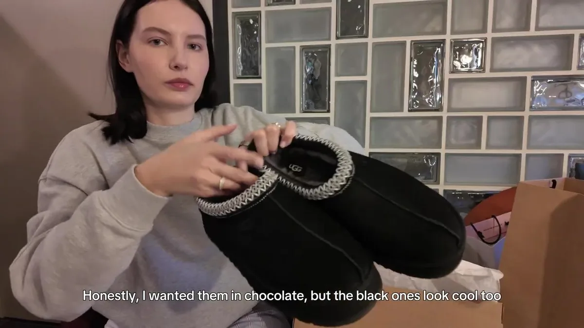 Me holding a pair of black UGG shoes with light braided edging.