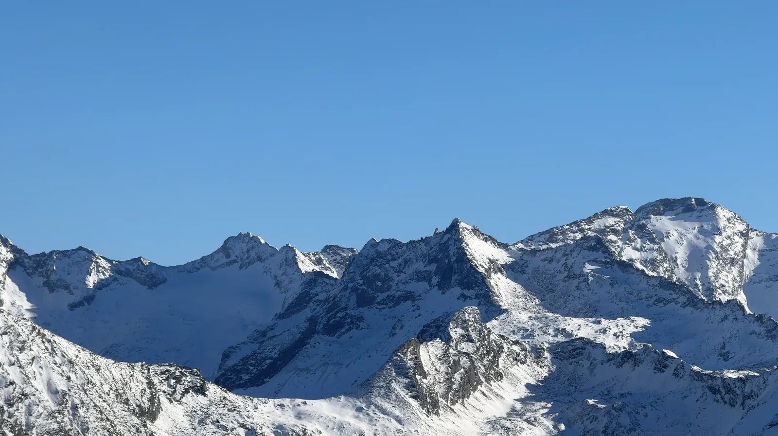 Rugged snow-covered mountain ridges beneath a clear blue sky.