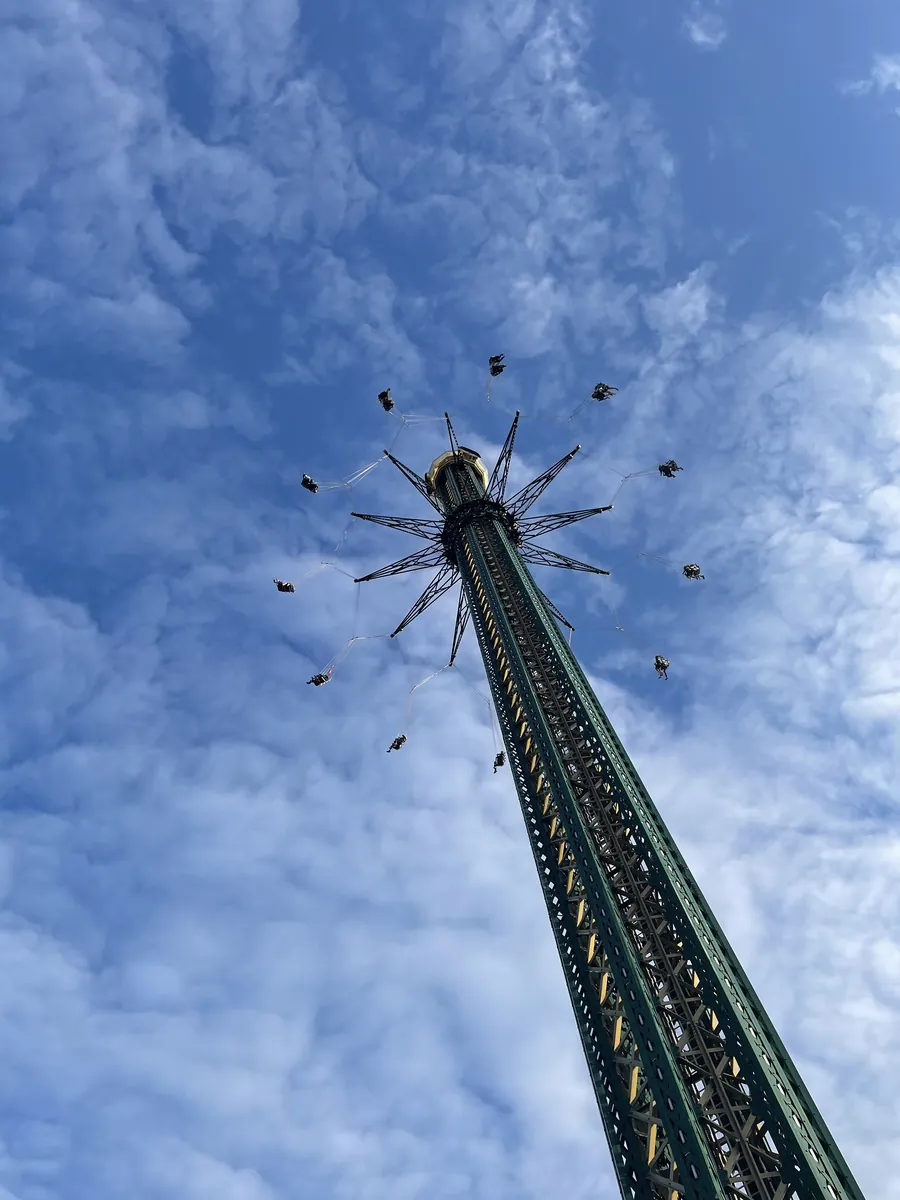 A tall swing ride with seats suspended against a blue sky